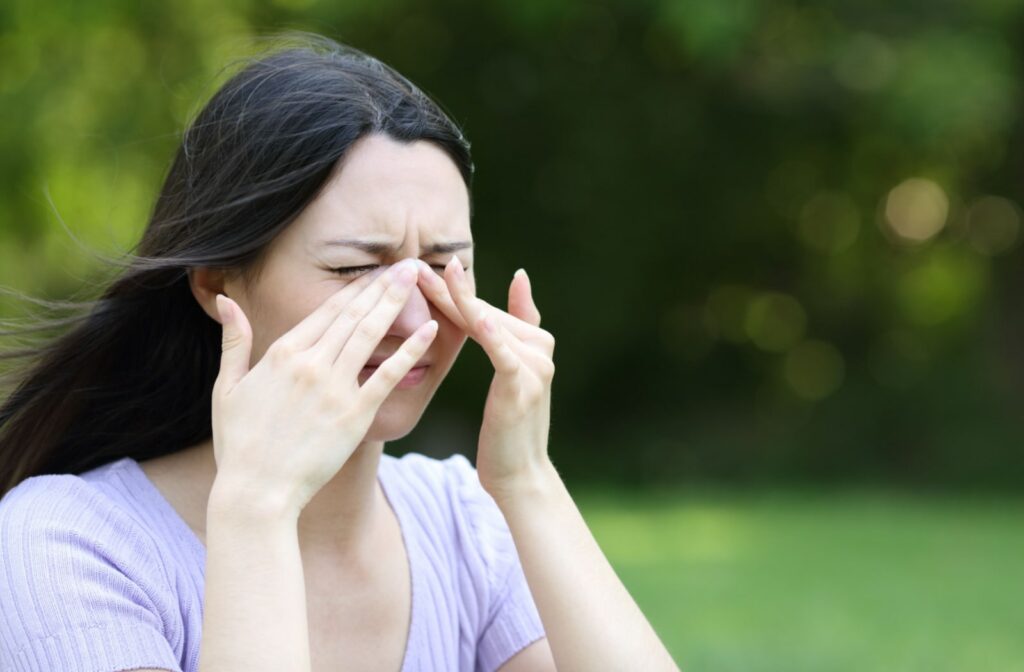 A woman rubs her dry eyes while standing outside