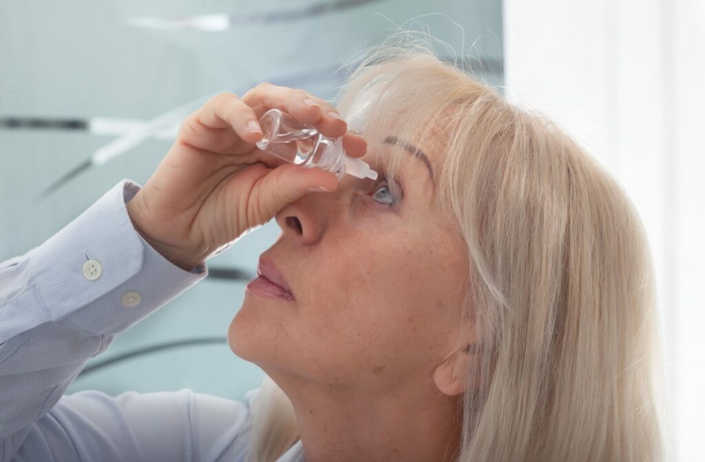 An older adult holds a bottle of artificial tears in her right hand over her left eye.