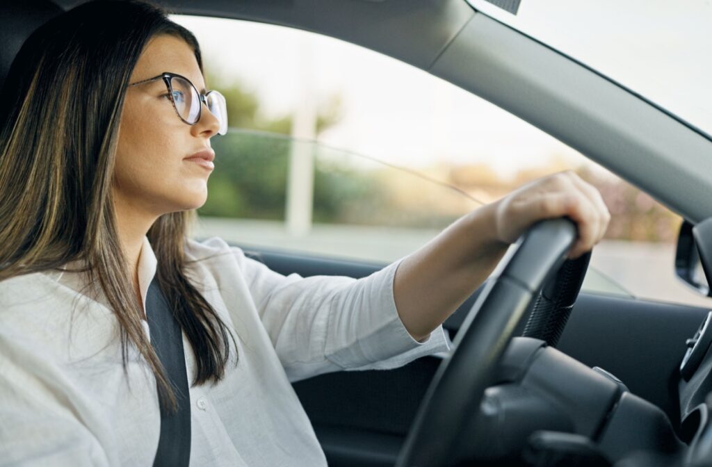 A person wearing glasses sits behind the steering wheel of their car.