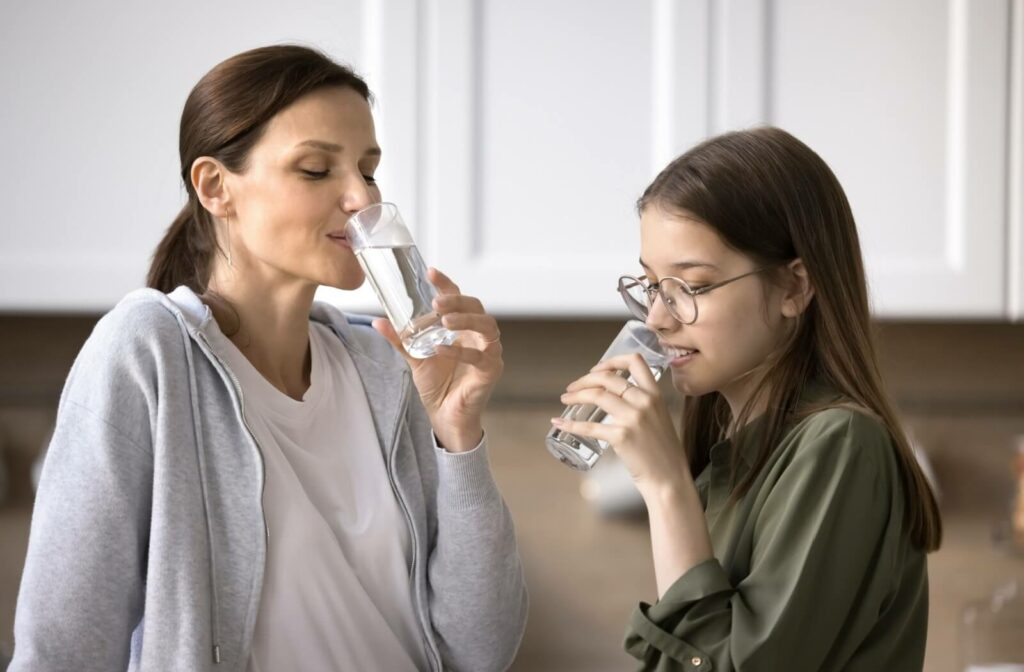  A parent and teenage child take a break in the kitchen to each drink a tall glass of water to keep their eyes hydrated