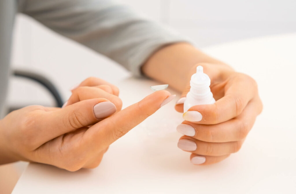 Close-up of hands holding a contact lens and a bottle of eye drops for hydration and comfort.