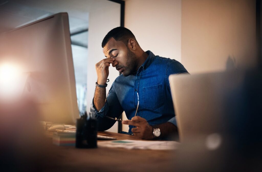 A person working at their computer rubs their sore eyes from digital eye strain.