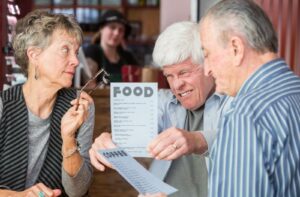 Three older adults struggling to read menus illustrating presbyopia and the need for reading glasses or vision correction.