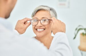 A smiling adult having glasses adjusted by an optometrist highlighting vision care solutions for presbyopia or hyperopia.