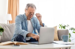 An older adult adjusting their glasses while looking at a computer screen due to early macular degeneration.