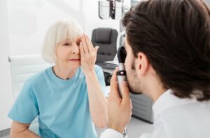 An older adult covering one eye with their hand during an eye exam to test for macular degeneration.