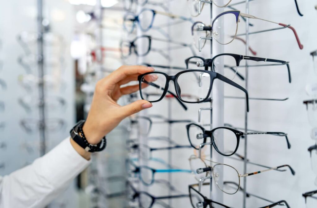 Many pairs of glasses sit on display, with one pair in someone's hand.