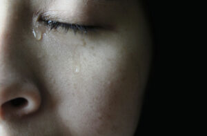 Close-up of a person's face with a tear running down their cheek, illustrating eye irritation or emotional tearing.
