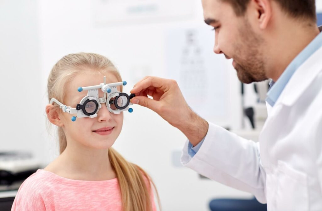 Optometrist adjusting a phoropter on a young girl during a pediatric eye exam in a clinical setting.
