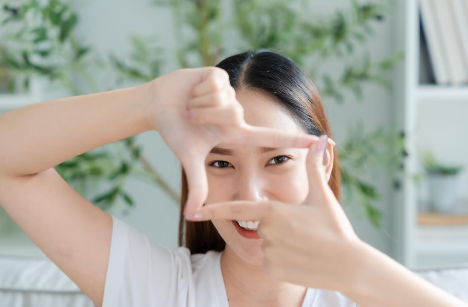Person smiling and forming a frame around their eyes with their hands, representing healthy vision.