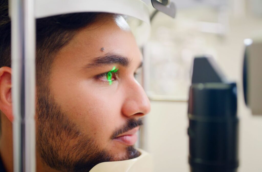 A close-up of a man’s eye being scanned with a green laser light during a diagnostic imaging test at an optometry clinic.