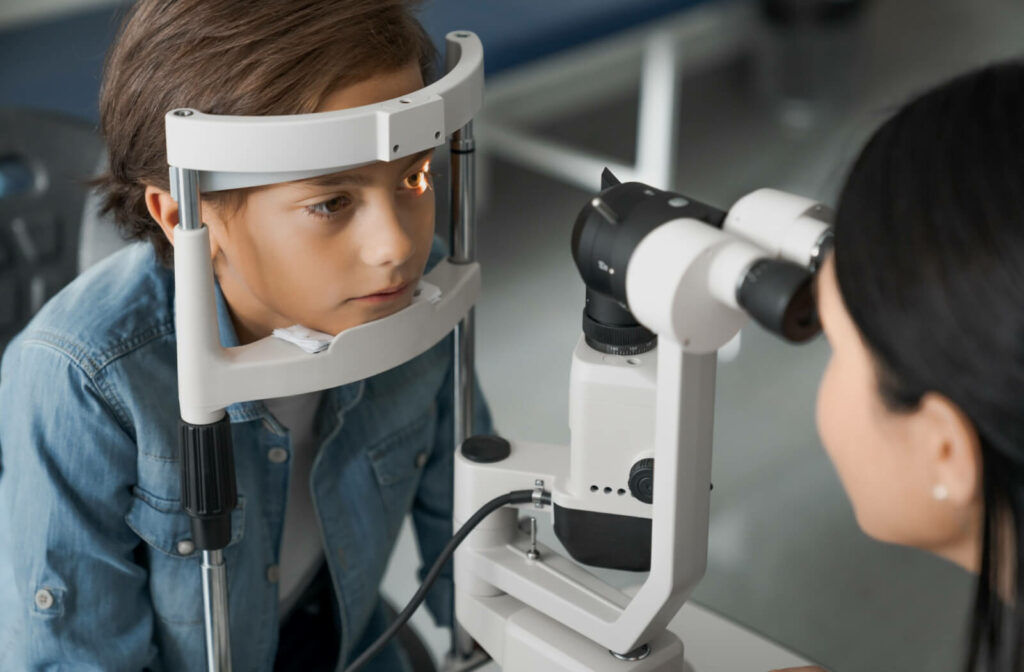 A young boy resting his chin on a slit lamp biomicroscope while an optometrist examines his eye structure during a pediatric myopia control evaluation.