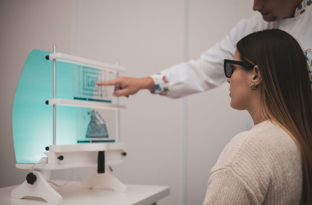 An adult woman wearing specialized polarized glasses during an in-office vision therapy session, as an optometric therapist points to a Brewster stereoscope training card to improve binocular eye coordination.