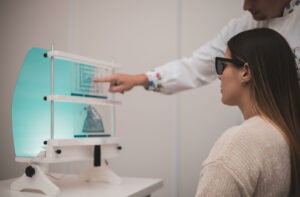 An adult woman wearing specialized polarized glasses during an in-office vision therapy session, as an optometric therapist points to a Brewster stereoscope training card to improve binocular eye coordination.